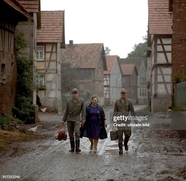 Zwei Grenzsoldaten der DDR-Grenztruppen der Nationalen Volksarmee der DDR tragen der Köchin Berta Niebel der Grenzeinheit Taschen und Einkaufsnetze...