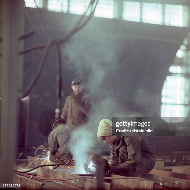 Eine Frau mit Kopftuch arbeitet als Elektro-Schweißerin auf der Warnow-Werft in Rostock-Warnemünde, aufgenommen im März 1967.