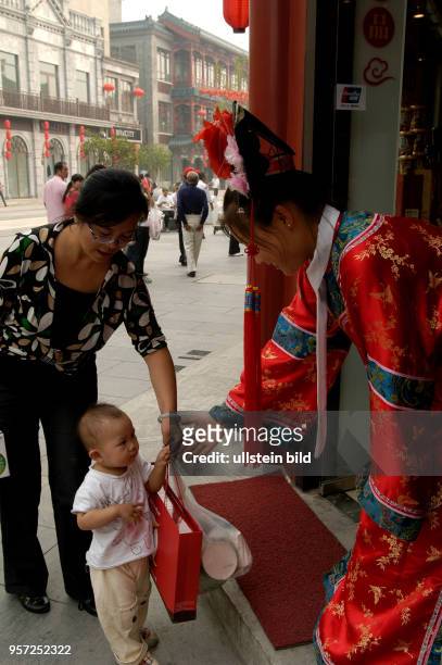 Oktober 2009 / China - Peking/ Eine Verkäuferin in traditioneller Kleidung begrüßt vor einem Geschäft in der sanierten alten Einkaufsstraße Qianmen...