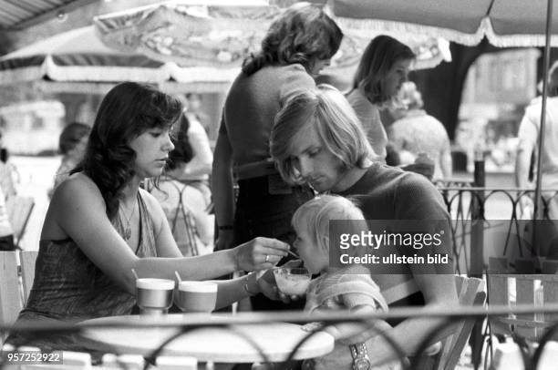 Junge Eltern sitzen mit ihrer kleinen Tochter in einemstraßen-Cafe in der Schönhauser Allee in Berlin Prenzlauer Berg, die Mutter füttert das Kind,...