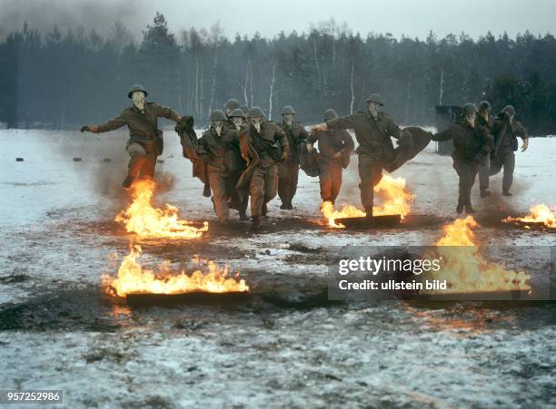 Infanteristen der Nationalen Volksarmee durchlaufen mit aufgesetzten Gasmasken im winterlichen Gelände bei einer Übung Feuer-Hindernisse, undatiertes...