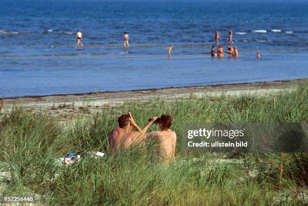 Ein Paar sitzt in den Dünen bei Peenemünde auf der Insel Usedom an der Ostsee und betrachtet Badende im Wasser, undatiertes Foto von 1991.