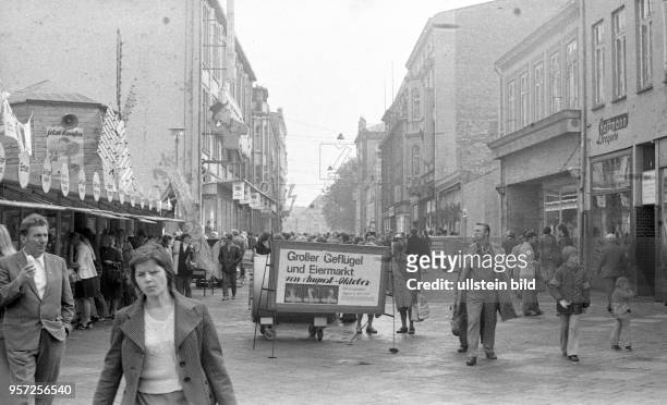 Menschen laufen in der Kröpeliner Strasse in der Innenstadt von Rostock, eine Werbetafel wibrt zum Einkauf auf einem Geflügel- und Eiermarkt,...