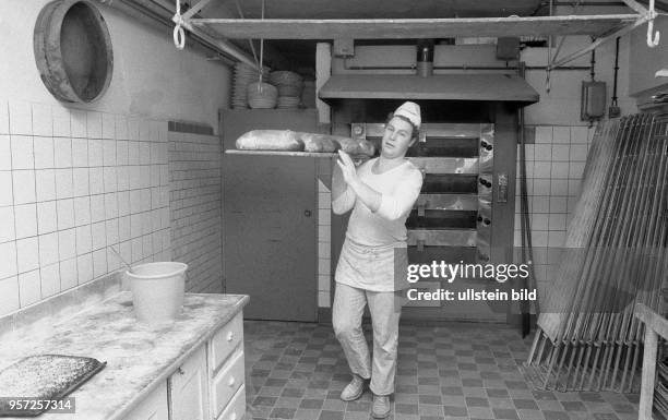 Bäckermeister Schmidt holt in seiner Bäckerei in Meiningen fertig gebackene Brote aus dem Ofen, aufgenommen 1986.