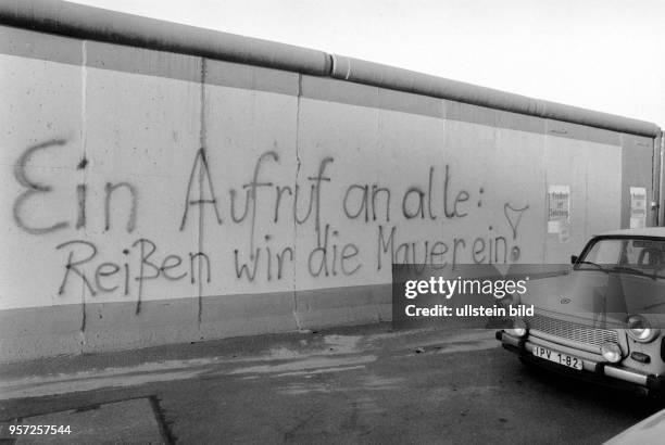 Ein Trabant fährt an einem mit dem Schriftzug "Ein Aufruf an alle: Reißen wird die Mauer ein!" versehenen Abschnitt der Berliner Mauer vorbei,...
