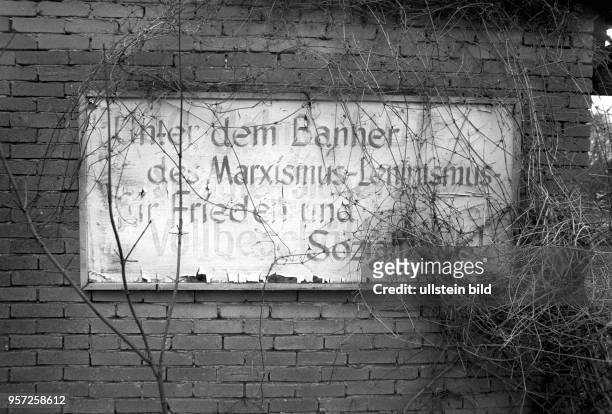 Eine verwitterte und mit Pflanzen überwachsene Tafel an einer alten Hauswand eines Gebäudes in Weferlingen im Grenzgebiet der DDR an der...