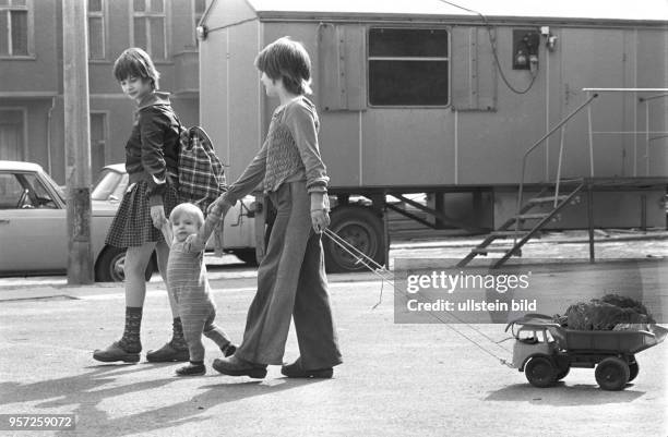 Zwei ältere Kinder unterstützen ein Kleinkind beim eigenständigen Laufen, aufgenommen im August 1977 im Berliner Stadtbezirk Prenzlauer Berg. Der...