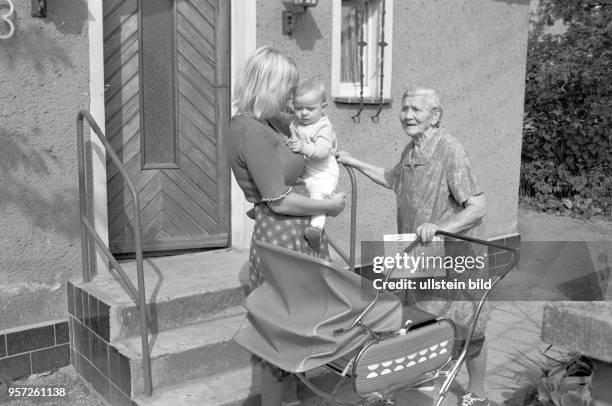 Eine junge Frau mit Kind und eine alte Frau mit einer Tageszeitung in der Hand stehen vor einem kleinen Einfamilienhaus in Magdeborn bei Leipzig,...