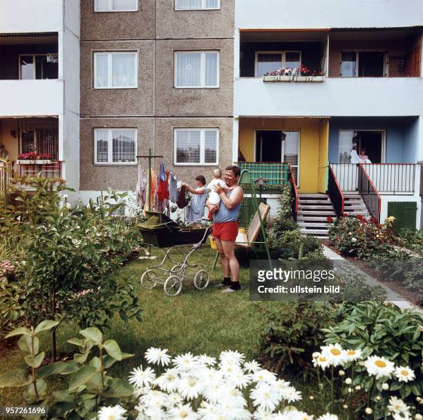 Ein Vater mit einem Kleinkind und eine Frau beim Wäscheaufhängen in einem kleinen Garten an einem Plattenbau im Neubaugebiet Halle-Neustadt,...