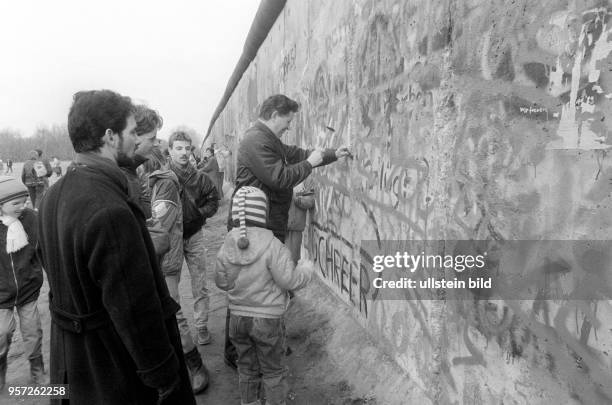 Ein Mann bearbeitet die Berliner Mauer auf West-Berliner Seite mit Hammer und Meißel, um kleine Bruchstücke aus dem Beton zu schlagen, die später zu...