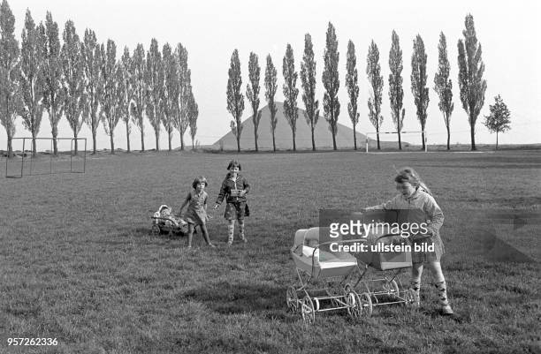 Mädchen spielen auf einem von Pappeln umsäumten Sportfeld mit ihren in Puppenwagen liegenden Puppen, aufgenommen zu Pfingsten am in Hübitz im...