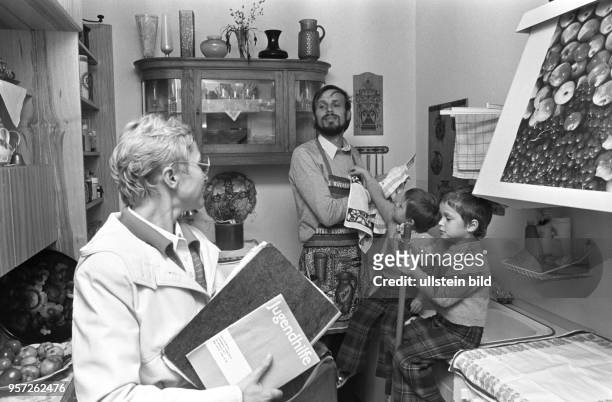 Eine Frau vom Amt besucht eine kinderreiche Familie in Berlin , der Hausherr steht mit einer Schürze bekleidet in der Küche und trocknet Geschirr ab,...