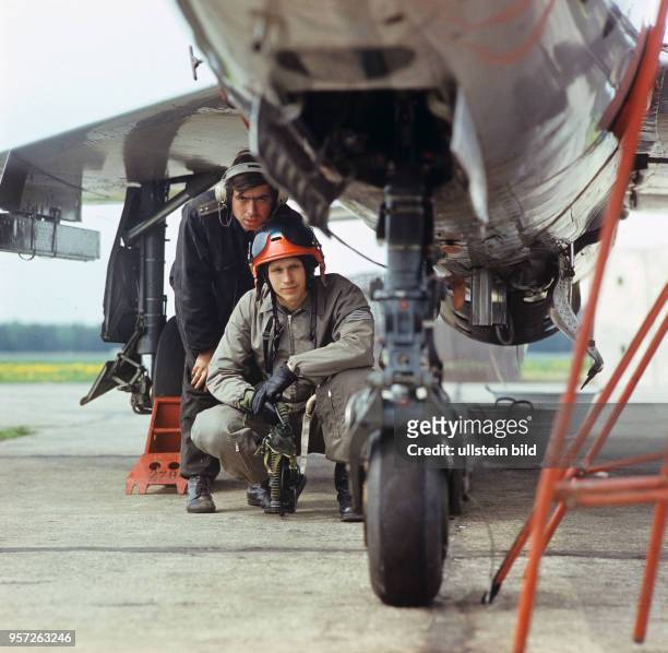 Der Offiziersschüler Reinhard Gräffe schaut mit einem Techniker auf das Fahrwerk eines Jagdflugzeugs MIG 21 vor seinem ersten Alleinflug miit diesem...