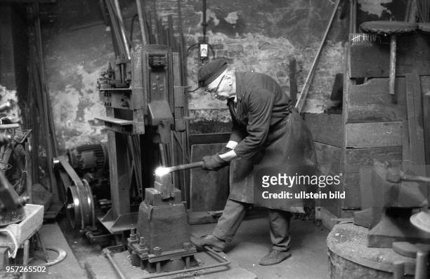 Ein Schmied bei der Arbeit in einer einfachen alten Werkstatt in einem Hinterhof eines Altbaus in der Nähe der Ackerstraße in Berlin-Mitte,...