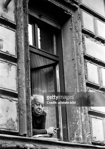 Ein älterer Mann schaut aus dem Fenster seiner Altbau-Wohnung im Berliner Stadtbezirk Prenzlauer Berg und raucht dabei eine Zigarette, aufgenommen...
