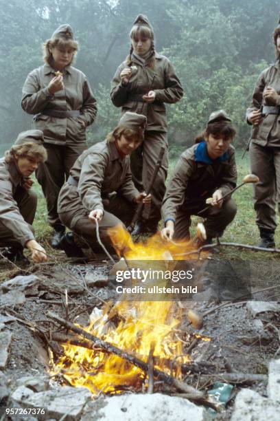 Junge Pädagogik-Studentinnen backen über einem Lagerfeuer Kartoffeln am Stock, undatiertes Foto von 1980. In Rahmen ihres Studiums müssen sie in...