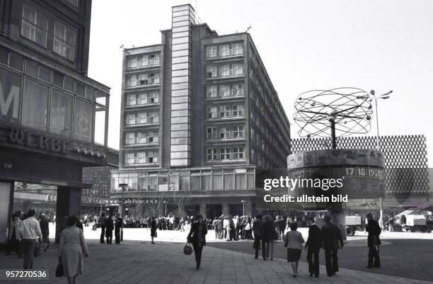 Menschen flanieren über den Berliner Alexanderplatz mit der von Erich John gestalteten Weltzeituhr, dem Berolinahaus und dem Centrum-Warenhaus ,...