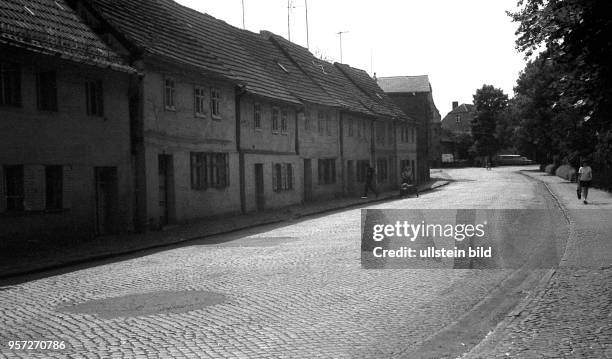 Eine Straße mit Kopfsteinpflaster gesäumt von allten Häusern mit dunklen Fassaden in der Altstadt von Jüterbog, undatiertes Foto aus den 1960er...