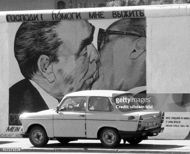 Ein Pkw Trabant steht an der Mühlenstrasse in Ostberlin vor dem Bild Bruderkuss , gemalt vom russischen Maler Dmitri Waldimirowitsch Wrubel ,...