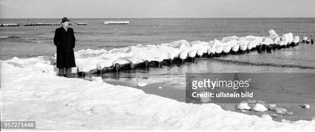 Ein Tourist mit Hut und Mantel vor einer vereisten Buhne am Strand vom Ostseebad Koserow auf der Insel Usedom im Winter 1957. Foto : Reinhard...