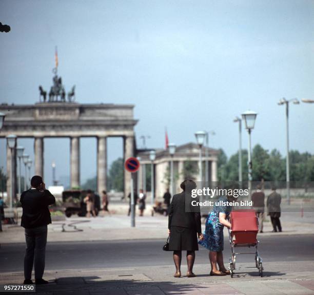 Ein fotografierender Mann und eine Frau mit Kinderwagen an der Straße Unter den Linden in Berlin , im Hintergrund das Brandenburger Tor, aufgenommen...