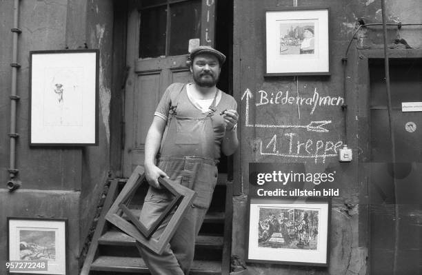 Ein Mann in Arbeitskleidung, mit Zigarre und Bilderrahmen in der Hand steht im Hinterhof eines Altbaus in der Nähe der Ackerstraße in Berlin-Mitte...