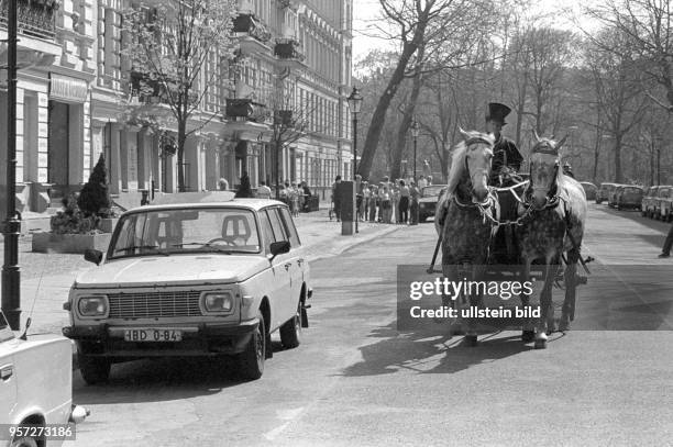 Berlin - Ein Pferdegespann mit einem Kutscher in historischer Kleidung passiert am Kollwitzplatz in Berlin , Prenzlauer Berg, die am Straßenrand...