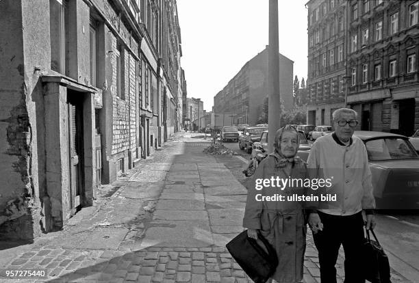 Ein altes Paar geht Hand in Hand mit Einkaufstaschen eine verfallene Straße in Berlin-Mitte in der Nähe der Ackerstraße entlang. Zwei Mädchen spielen...