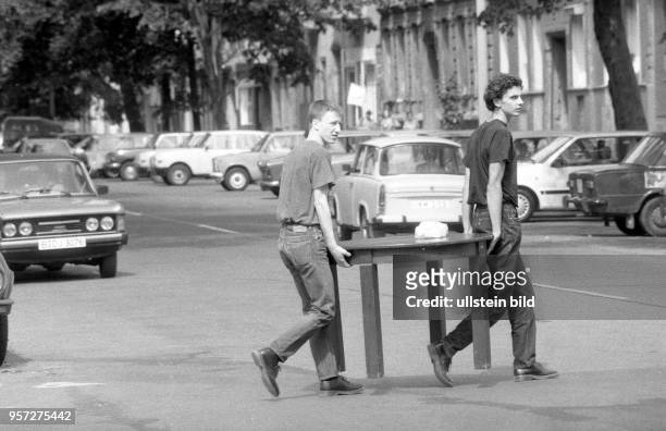 Zwei junge Männer tragen einen Tisch über eine Strasse am Kollwitzplatz in Ostberlin, aufgenommen im Sommer 1990.