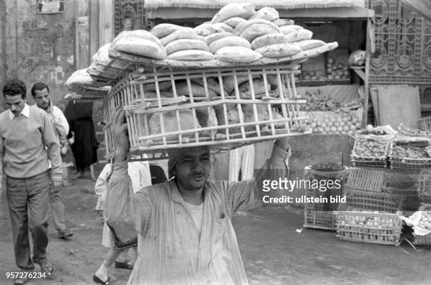 Ein Bäcker trägt einen geflochtenen Korb mit Fladenbrot auf dem Kopf zu einem Verkaufsstand auf einen Basar in Kairo , aufgenommen 1972.