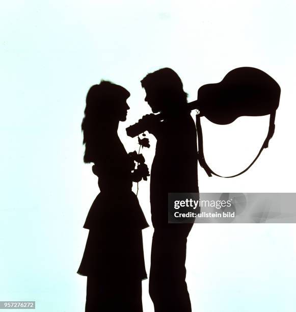 Ein als Silhouette gestaltetes Foto zeigt ein junges Mädchen mit einer Rose und einen jungen Mann mit Gitarre, undatiertes Foto von 1978. Die...