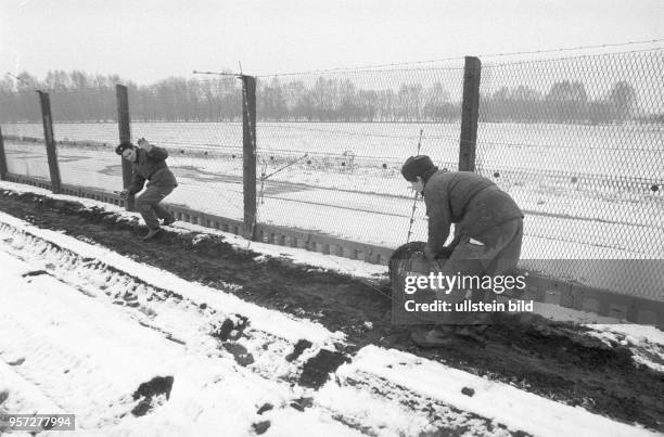 Grenzer der Nationalen Volksarmee bauen am Metallzaun der innerdeutschen Grenze in verschneiter Landschaft bei Salzwedel Stacheldraht ab, aufgenommen...