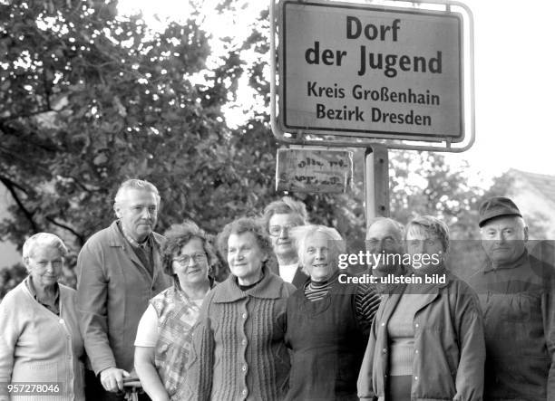 Im August 1990 stehen Senioren am Ortsschild des "Dorfes der Jugend" im Kreis Großenhain im Bezirk Dresden, dazwischen die Bürgermeisterin des Dorfes...