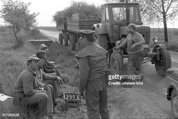 Eine Gruppe von Männern sitzt am Straßenrand und trinkt Bier, aufgenommen zu Pfingsten am in Hübitz im Mansfelder Land. Rechts ein Traktorist vor...