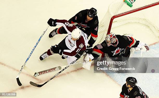 Cam Ward of the Carolina Hurricanes looks to make a poke save as teammate Aaron Ward checks Matt Hendricks of the Colorado Avalanche during a NHL...