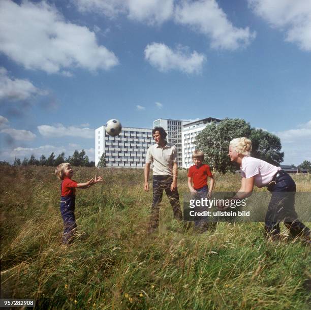 Eine Familie mit zwei Kindern beim Ballspielen auf einer Wiese vor dem Neubau eines FDGB-Erholungsheimes in Waren-Klink an der Müritz, undatiertes...