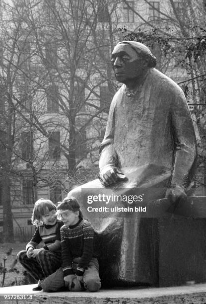 Zwei Kinder sitzen auf dem Sockel zu Füßen des Denkmals von Käthe Kollwitz auf dem Ko1lwitzplatz in Berlin , Prenzlauer Berg, aufgenommen im Frühjahr...