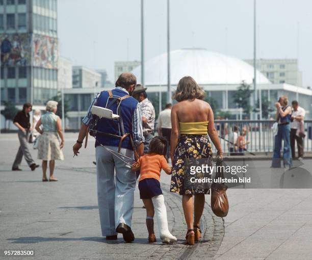 Eine Familie läuft mit einem Jungen mit Gipsbein über den Alexanderplatz in Berlin, im Hintergrund die Kongreßhalle am Haus des Lehrers, aufgenommen...