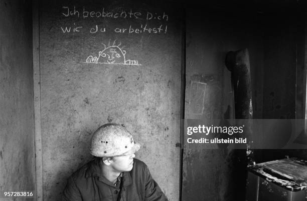 Ein Arbeiter der August-Bebel-Hütte Helbra macht eine Pause und sitzt unter einem mit Kreide an der Wand angebrachten Schriftzug "Ich beobachte Dich...