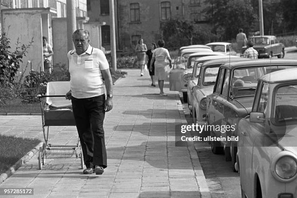 Ein alter Mann mit Kinderwagen im Neubaugebiet in der Helbraer Straße in der Lutherstadt Eisleben , aufgenommen im Juni 1983. Am Straßenrand sind Pkw...