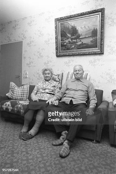 Ein älteres Ehepaar auf dem Sofa in ihrer Neubauwohnung in einem Plattenbau im Wohngebiet Ernst-Thälmann-Park in Berlin , aufgenommen 1985. Über dem...