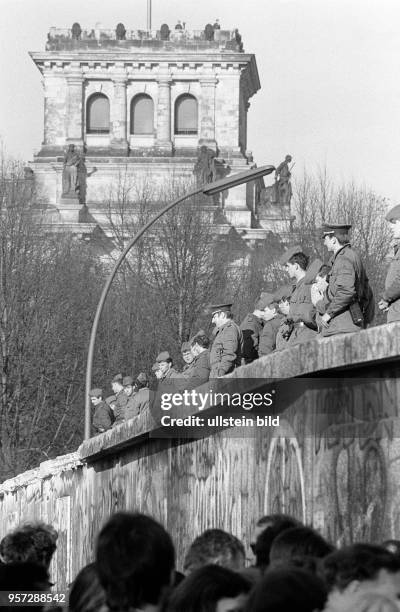 Soldaten der DDR-Grenztruppen stehen am auf einem Mauerabschnitt nahe des Reichstagsgebäudes in Berlin. Die Grenzöffnung, bzw. Der Mauerfall, war am...