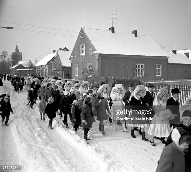 Durch das winterlich verschneite Dorf Werben ziehen junge Paare in Tracht beim niedersorbisch Fastnachtumzug Zapust im Februar 1969.