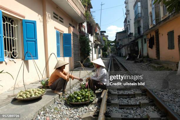 Zwei Straßenhändler sitzen am Schotterbett eines Gleises in einer engen Gasse in der Altstadt von Hanoi, der Hauptstadt der Sozialistischen Republik...