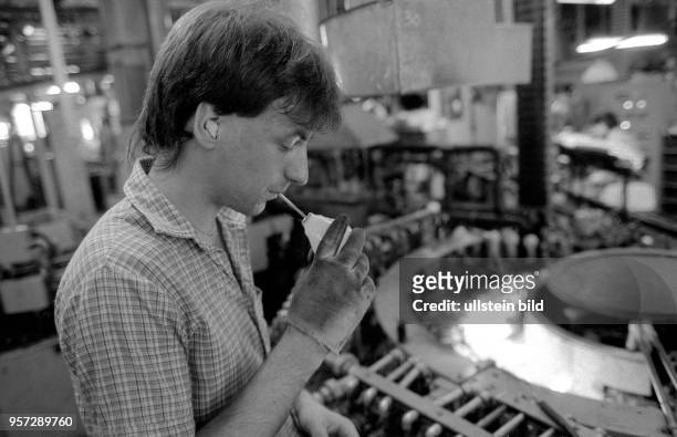 Ein Mitarbeiter des VEB Kombinat NARVA kontrolliert den Glaskörper einer hergestellten Glühlampe auf seine Qualität, aufgenommen 1989 in Berlin.