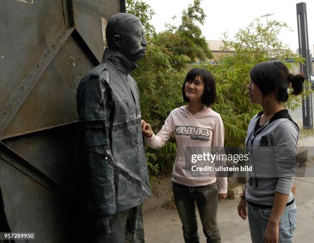 Oktober 2009 / China - Peking / Zwei junge Mädchen stehen am Eingang zu einer Ausstellungshalle und betrachten eine Figur. Kunst spielt in Peking,...