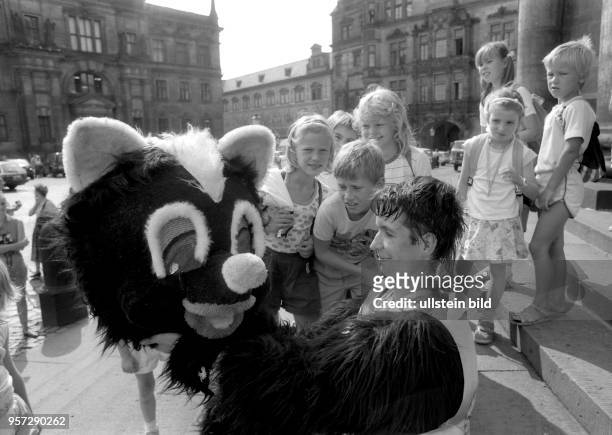 Ein Mann im Bärenkostüm hat den Kopf seiner Verkleidung abgesetzt und präsentiert diesen einer Gruppe Schulkinder, aufgenommen im August 1990 auf dem...