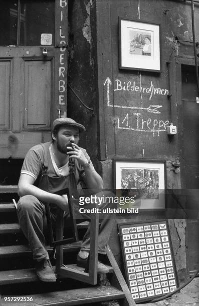 Ein Mann in Arbeitskleidung, mit Zigarre und Bilderrahmen in der Hand sitzt im Hinterhof eines Altbaus in der Nähe der Ackerstraße in Berlin-Mitte...