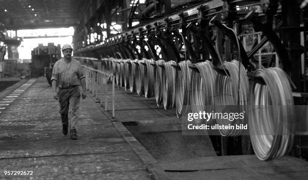 Ein Arbeiter läuft an Rollen von Stahldraht entlang, aufgenommen im Sommer 1989 im Stahl- und Walzwerk Hennigsdorf..