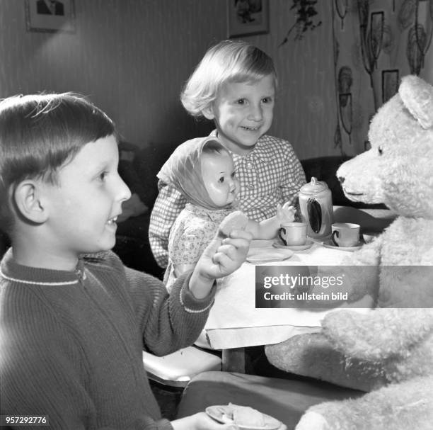 Ein kleines Mädchen und ein kleiner Junge spielen mit Puppe und Teddybär "Familienfrühstück", Foto vom .